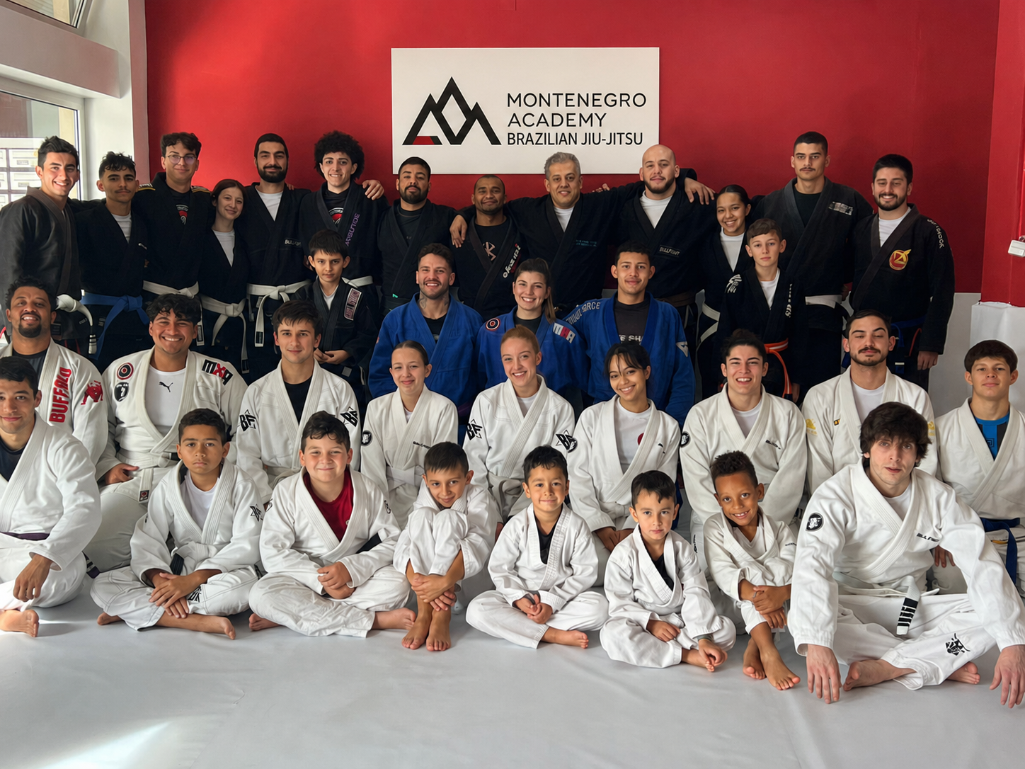 Grupo grande de alunos da academia, adultos e crianças, reunidos no tatame